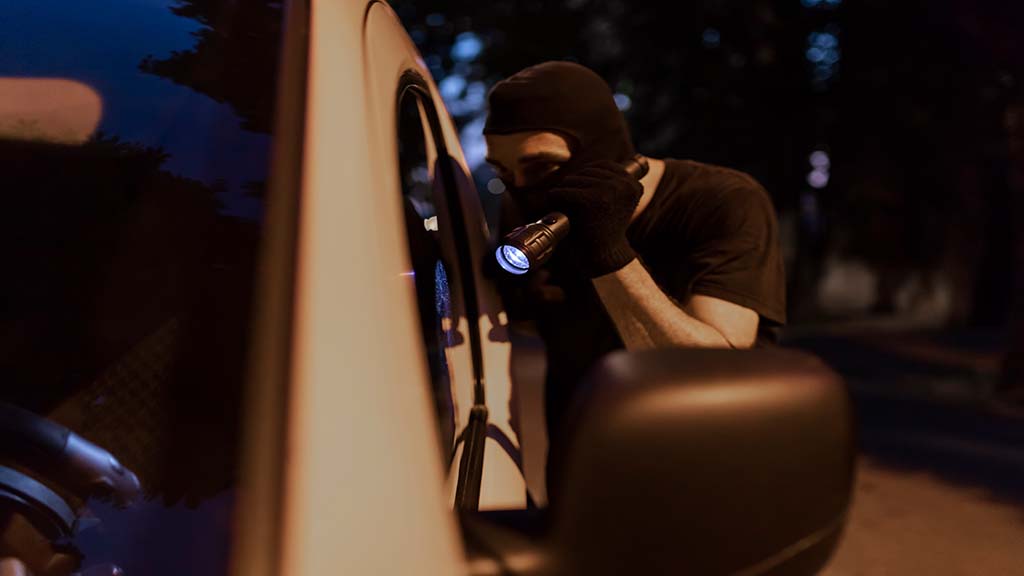 En tjuv med ficklampa och mask som försöker stjäla en bil utan tonade rutor